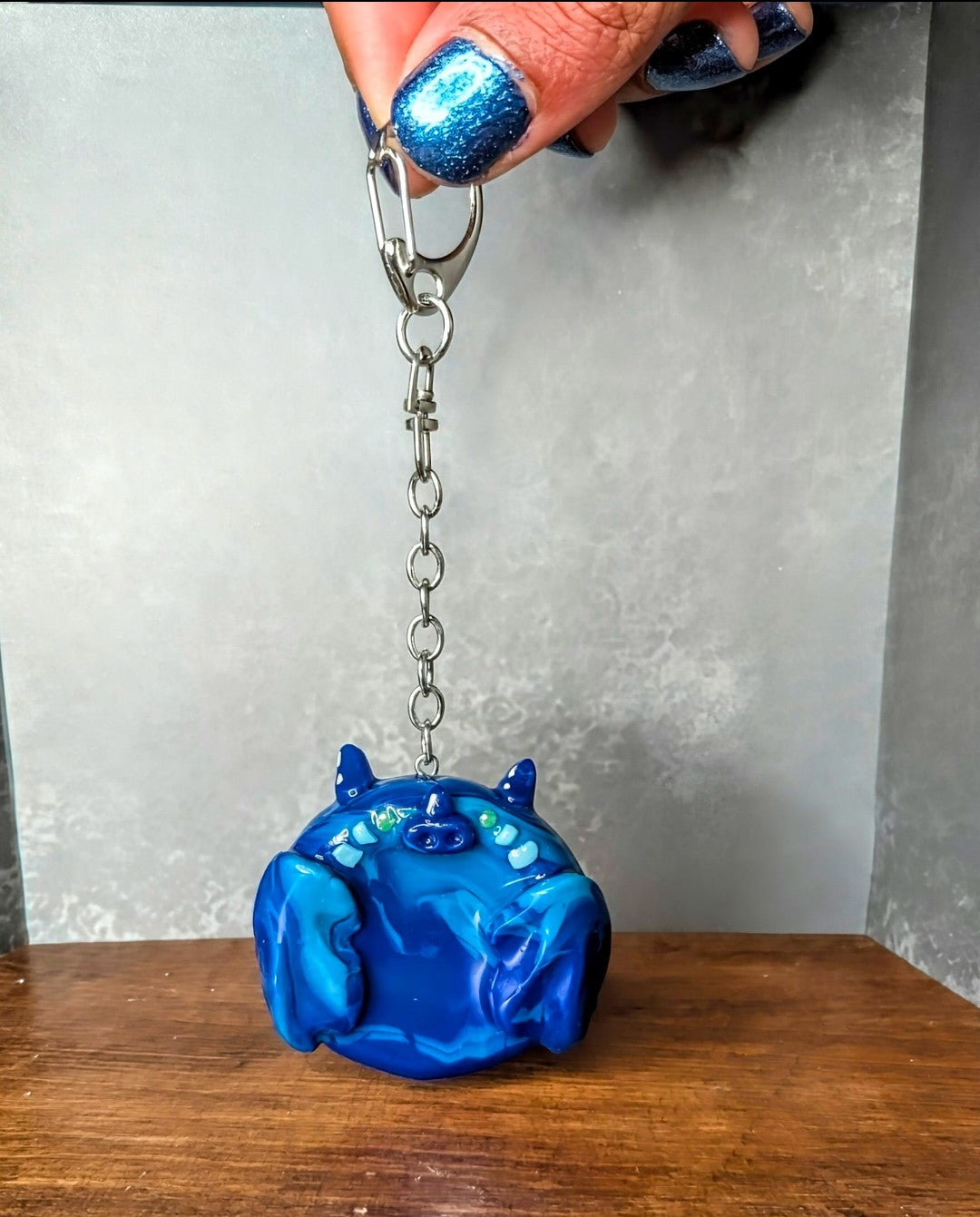 Blue dragon-shaped keychain held by a hand with blue nail polish against a neutral background Handcrafted sea dragon worry stone in blue ocean-toned gemstone